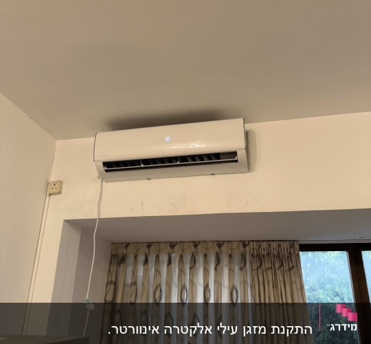 מזגן מותקן על קיר מעל חלון עם וילון